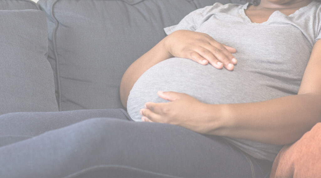 Pregnant woman of color laying on couch holding her belly