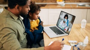 Photo of a father and son using a telehealth doctor out of their home