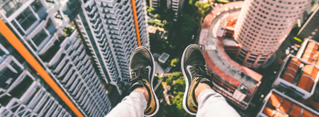 person sitting on a tall building with their feet hanging off the edge